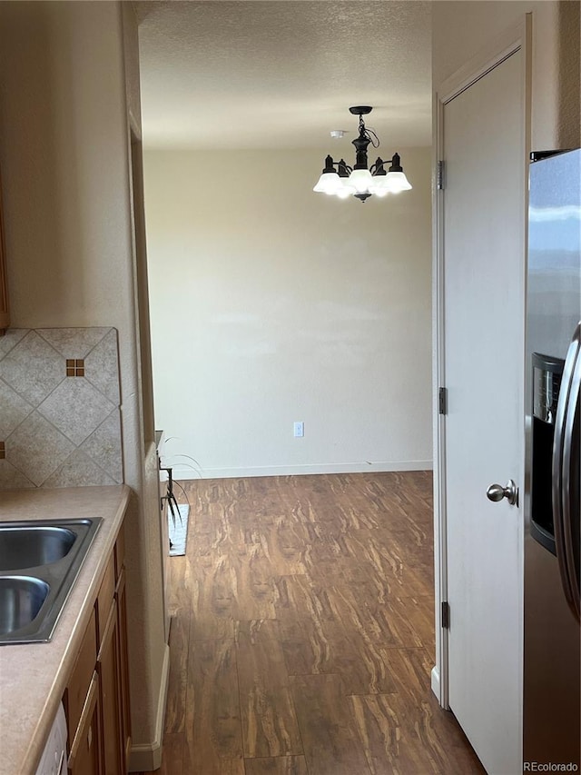 kitchen with decorative backsplash, sink, hanging light fixtures, dark wood-type flooring, and stainless steel fridge