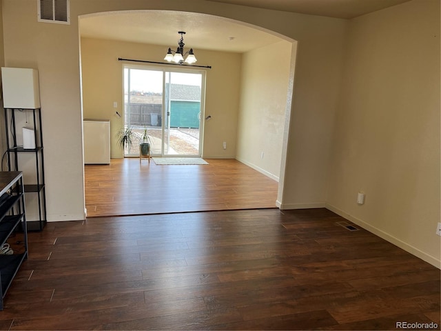 empty room with dark hardwood / wood-style floors and a notable chandelier