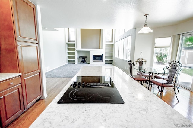17672 E Weaver Pl, Aurora, CO 80016 - kitchen featuring black electric stovetop, light countertops, light wood finished floors, and a glass covered fireplace