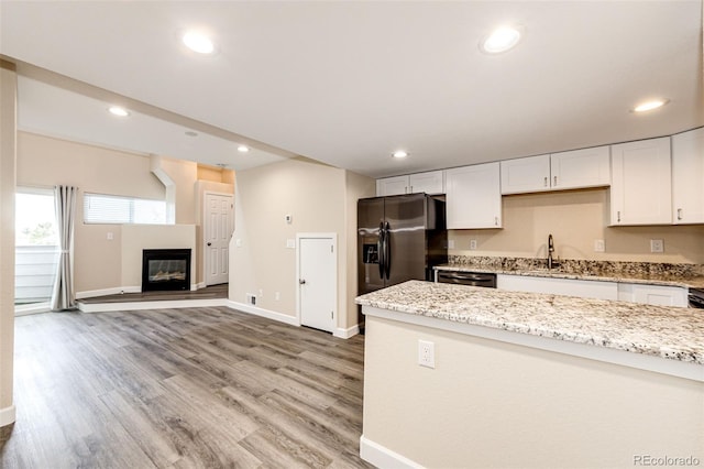 kitchen featuring stainless steel refrigerator with ice dispenser, light stone counters, white cabinets, baseboards, and dishwasher