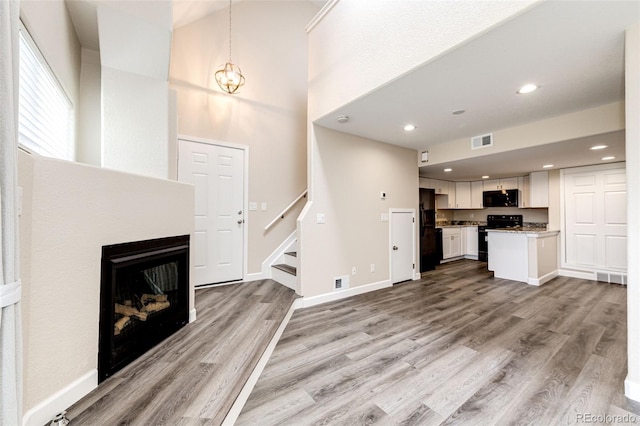 unfurnished living room with stairs, light wood finished floors, a fireplace, a high ceiling, and recessed lighting