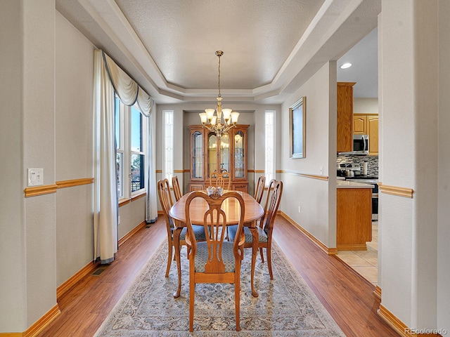 dining area featuring a raised ceiling, an inviting chandelier, light hardwood / wood-style flooring, and plenty of natural light