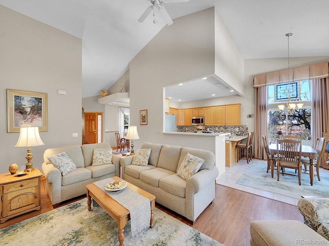 living room with ceiling fan with notable chandelier, high vaulted ceiling, and light hardwood / wood-style flooring