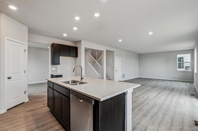 kitchen with sink, light stone counters, stainless steel dishwasher, an island with sink, and light hardwood / wood-style floors