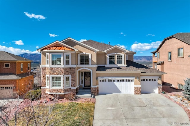 traditional-style home with stone siding, a mountain view, concrete driveway, and stucco siding