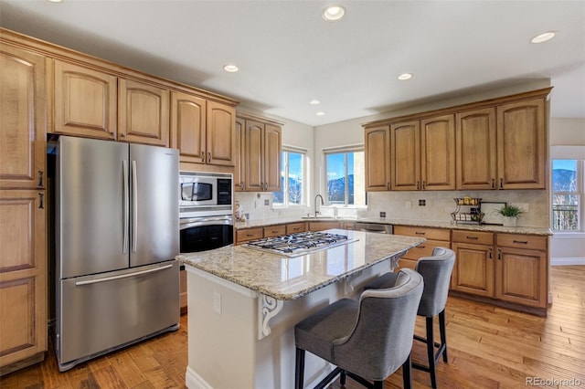 kitchen with light stone counters, appliances with stainless steel finishes, a kitchen breakfast bar, light wood-style floors, and a sink