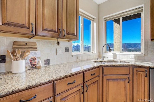 kitchen featuring light stone counters, brown cabinets, a sink, and decorative backsplash