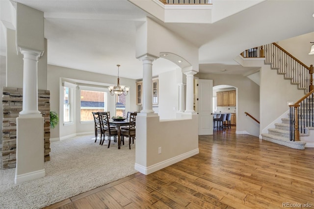 foyer entrance featuring ornate columns, stairway, an inviting chandelier, wood finished floors, and baseboards