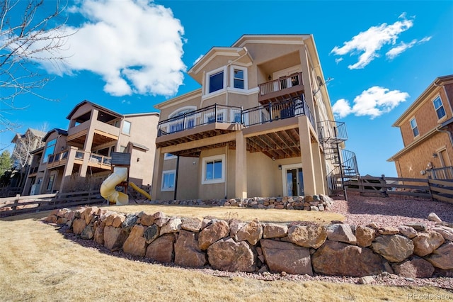 back of house featuring fence, a balcony, and stucco siding