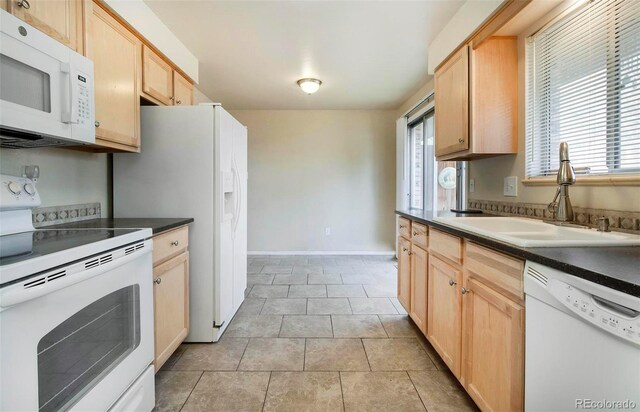 kitchen featuring light brown cabinets, a sink, dark countertops, white appliances, and light tile patterned floors