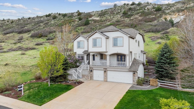 traditional-style home with driveway, a front yard, fence, an attached garage, and stone siding