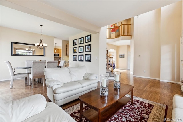 living room featuring arched walkways, a notable chandelier, baseboards, and wood finished floors