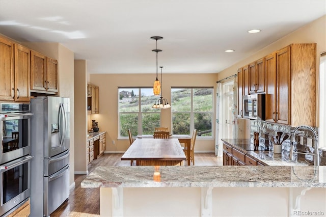 kitchen featuring brown cabinets, wood finished floors, baseboards, a kitchen island, and appliances with stainless steel finishes
