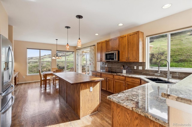 kitchen featuring a sink, brown cabinetry, stainless steel appliances, and light stone counters