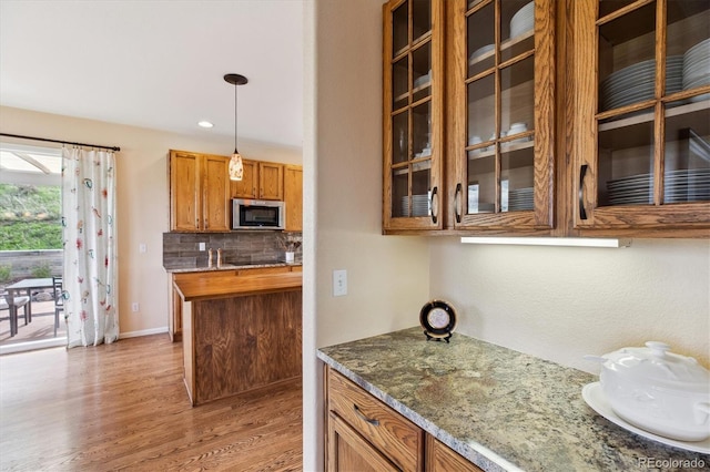 kitchen with glass insert cabinets, brown cabinetry, stainless steel microwave, light wood-style floors, and tasteful backsplash