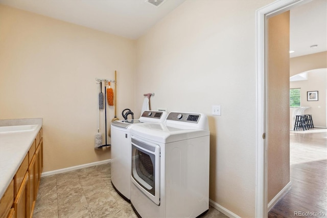 laundry area featuring cabinet space, washer and clothes dryer, visible vents, baseboards, and arched walkways
