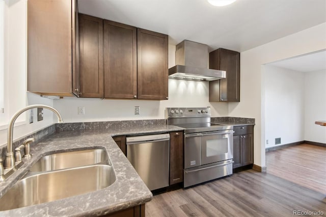 kitchen with wall chimney range hood, sink, light hardwood / wood-style flooring, appliances with stainless steel finishes, and dark brown cabinetry