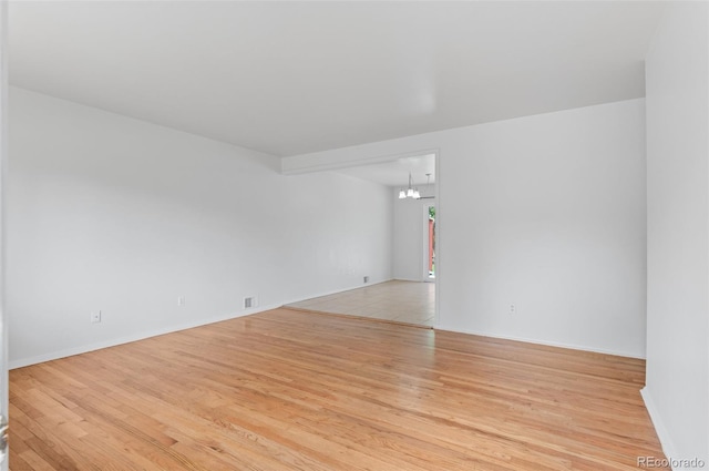 unfurnished room featuring a chandelier, light wood-style floors, and baseboards