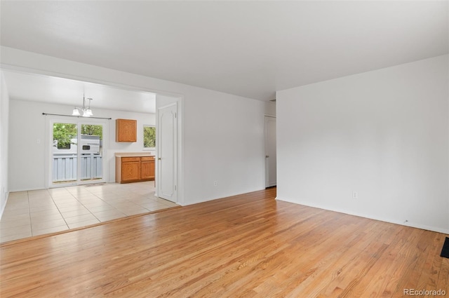 unfurnished living room with a chandelier, light wood-style floors, and baseboards