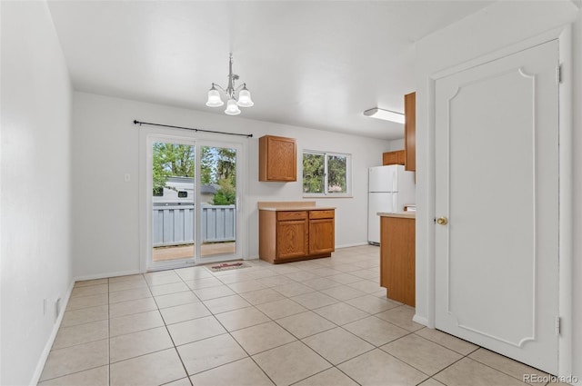 kitchen featuring freestanding refrigerator, light countertops, a chandelier, brown cabinetry, and decorative light fixtures
