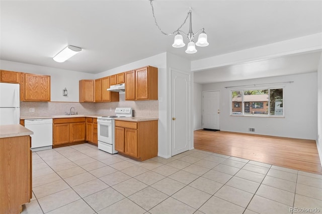kitchen with white appliances, under cabinet range hood, light tile patterned floors, and light countertops