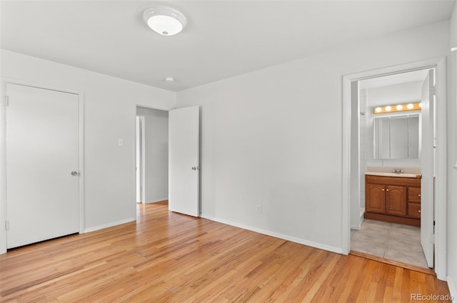 unfurnished bedroom with light wood finished floors, baseboards, ensuite bath, and a sink