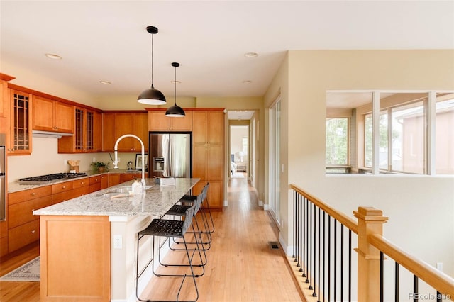 2940 Ulster St, Denver, CO 80238 - kitchen with stainless steel appliances, light wood-type flooring, brown cabinets, a breakfast bar, and glass insert cabinets