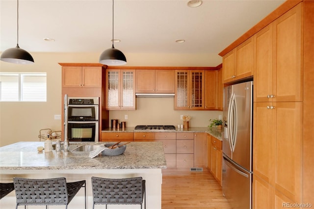 2940 Ulster St, Denver, CO 80238 - kitchen with appliances with stainless steel finishes, light wood-type flooring, light stone counters, glass insert cabinets, and decorative light fixtures