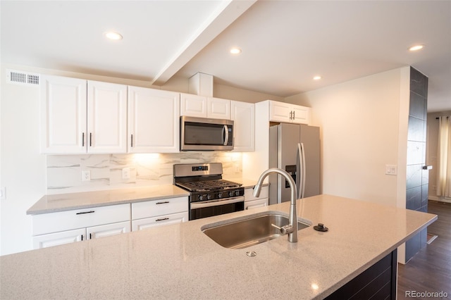 kitchen featuring tasteful backsplash, light stone counters, white cabinets, stainless steel appliances, and a sink