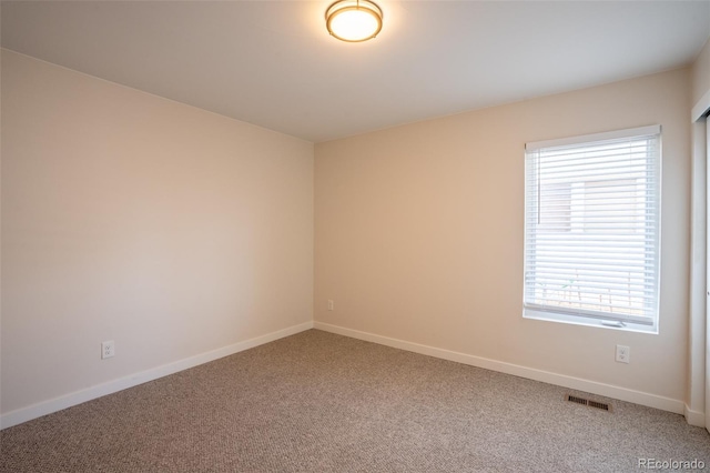 empty room with visible vents, a wealth of natural light, and carpet flooring