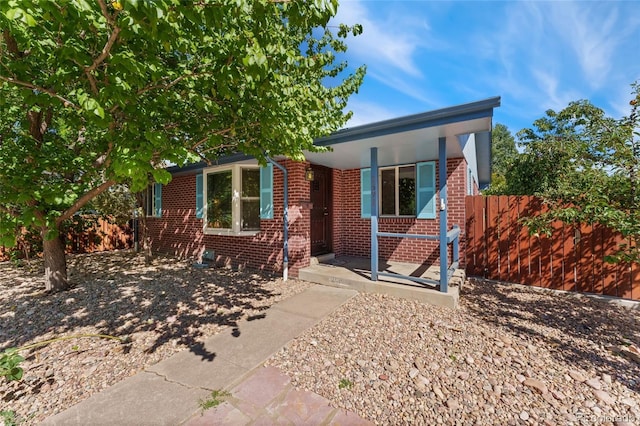 view of front of home featuring a porch, brick siding, and fence