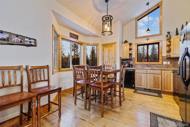 dining space featuring plenty of natural light, light wood-type flooring, sink, and high vaulted ceiling