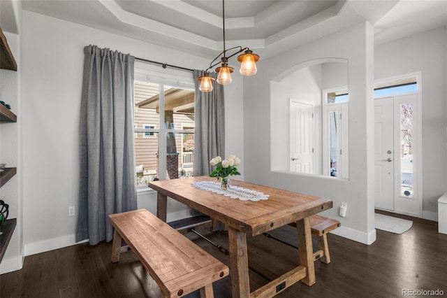 dining room featuring arched walkways, a raised ceiling, dark wood finished floors, and baseboards