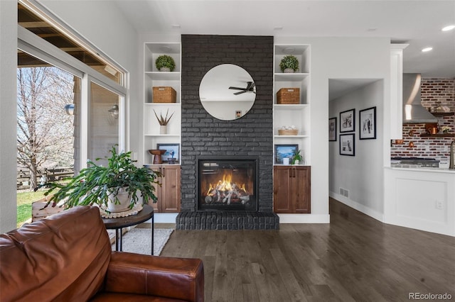 living area with built in shelves, a brick fireplace, wood finished floors, baseboards, and recessed lighting