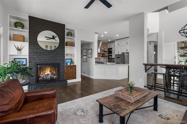 living room with a ceiling fan, built in shelves, wood finished floors, a fireplace, and recessed lighting