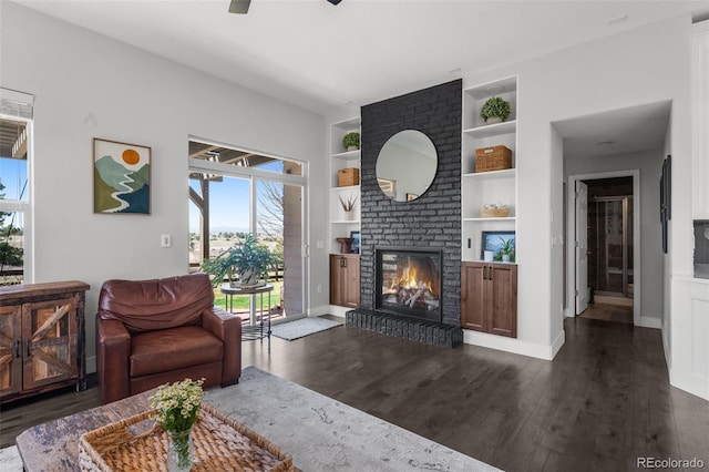 living area with built in features, dark wood-type flooring, a brick fireplace, and baseboards