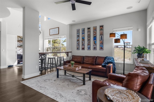 living area featuring a ceiling fan, baseboards, wood finished floors, plenty of natural light, and a high ceiling
