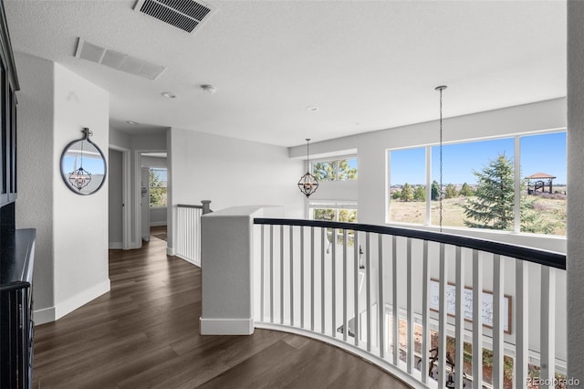 corridor with an upstairs landing, dark wood-style flooring, plenty of natural light, and baseboards