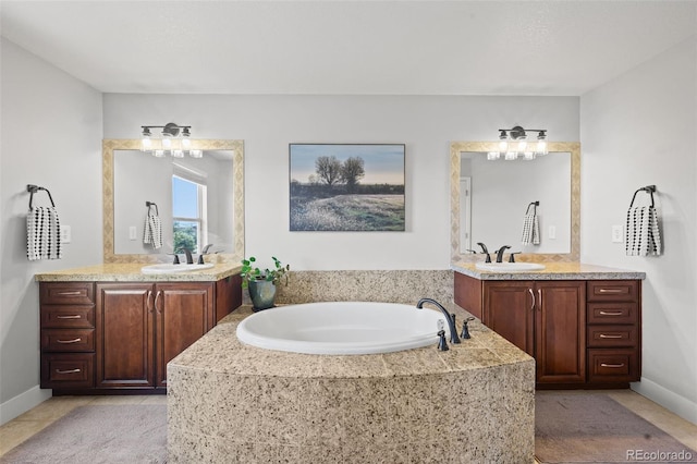 full bath with two vanities, a bath, and baseboards