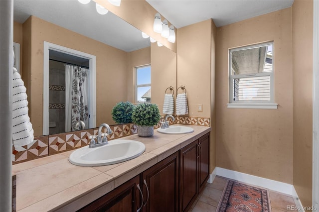 full bath featuring healthy amount of natural light, baseboards, double vanity, and tile patterned floors