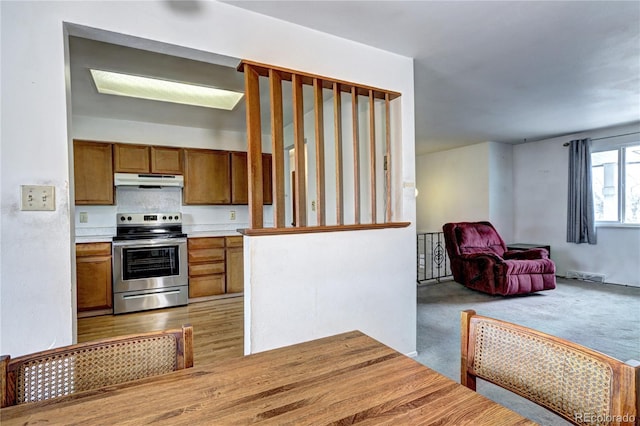 kitchen featuring carpet, stainless steel electric range, light countertops, under cabinet range hood, and brown cabinets