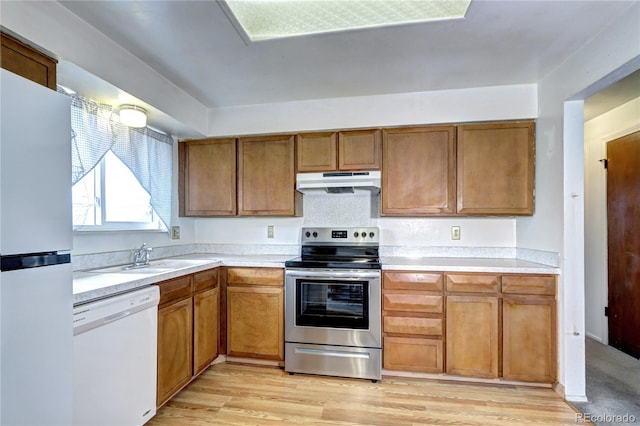 kitchen featuring under cabinet range hood, light countertops, brown cabinets, white appliances, and a sink