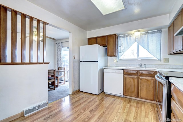 kitchen with visible vents, light countertops, light wood-style flooring, white appliances, and a sink