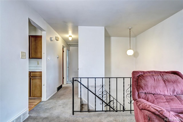 sitting room with baseboards, an upstairs landing, visible vents, and light carpet