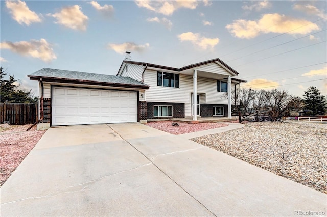 view of front of house featuring a garage, fence, brick siding, and driveway