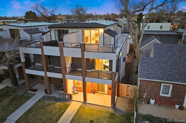 rear view of property with fence, stucco siding, a patio area, a balcony, and a yard