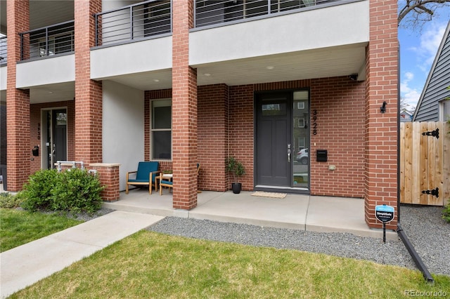 entrance to property featuring fence, covered porch, stucco siding, and brick siding