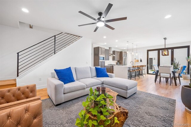 living area with light wood-type flooring, recessed lighting, ceiling fan, and stairway