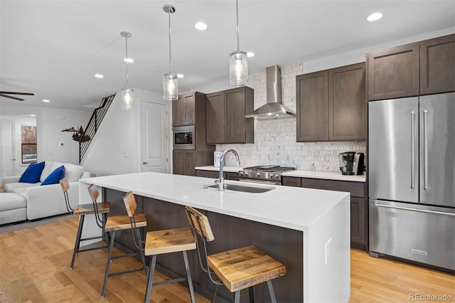 kitchen with dark brown cabinets, a sink, wall chimney exhaust hood, stainless steel appliances, and open floor plan