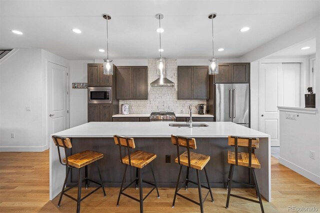 kitchen with a sink, wall chimney range hood, dark brown cabinetry, and stainless steel appliances